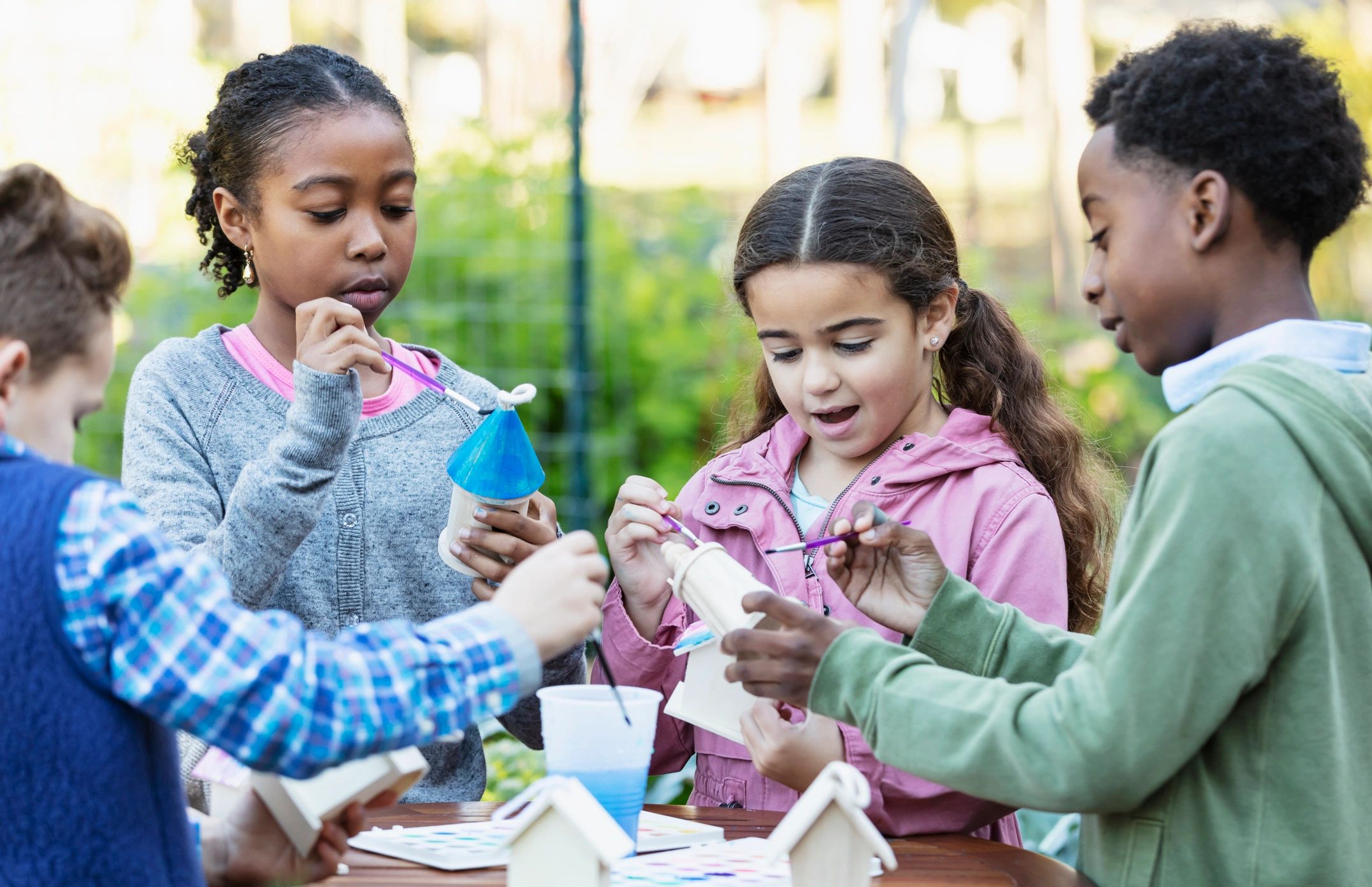 Children painting birdhouses together during an outdoor art activity
