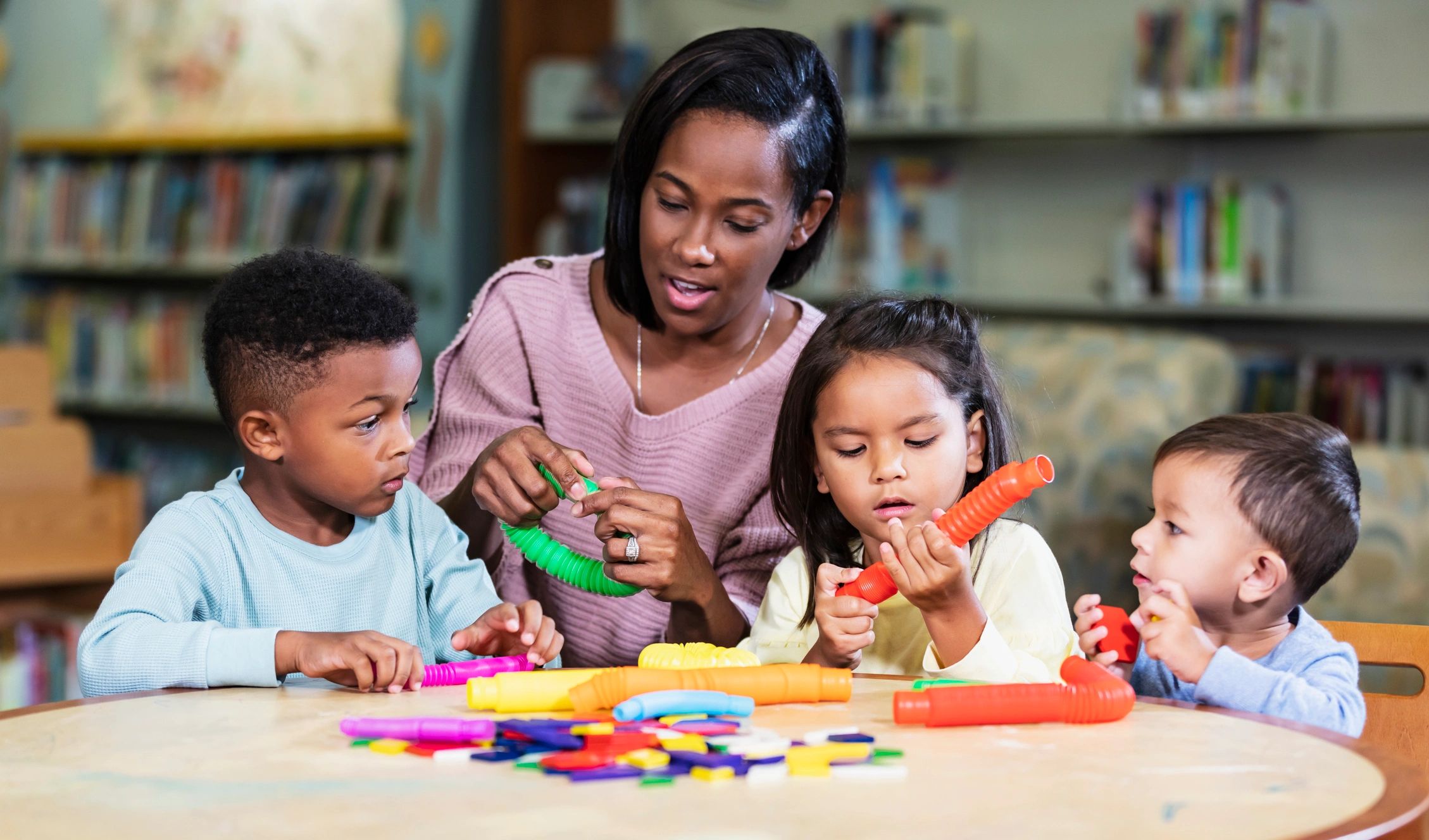 Caregiver playing with preschool children using colorful toys at a table