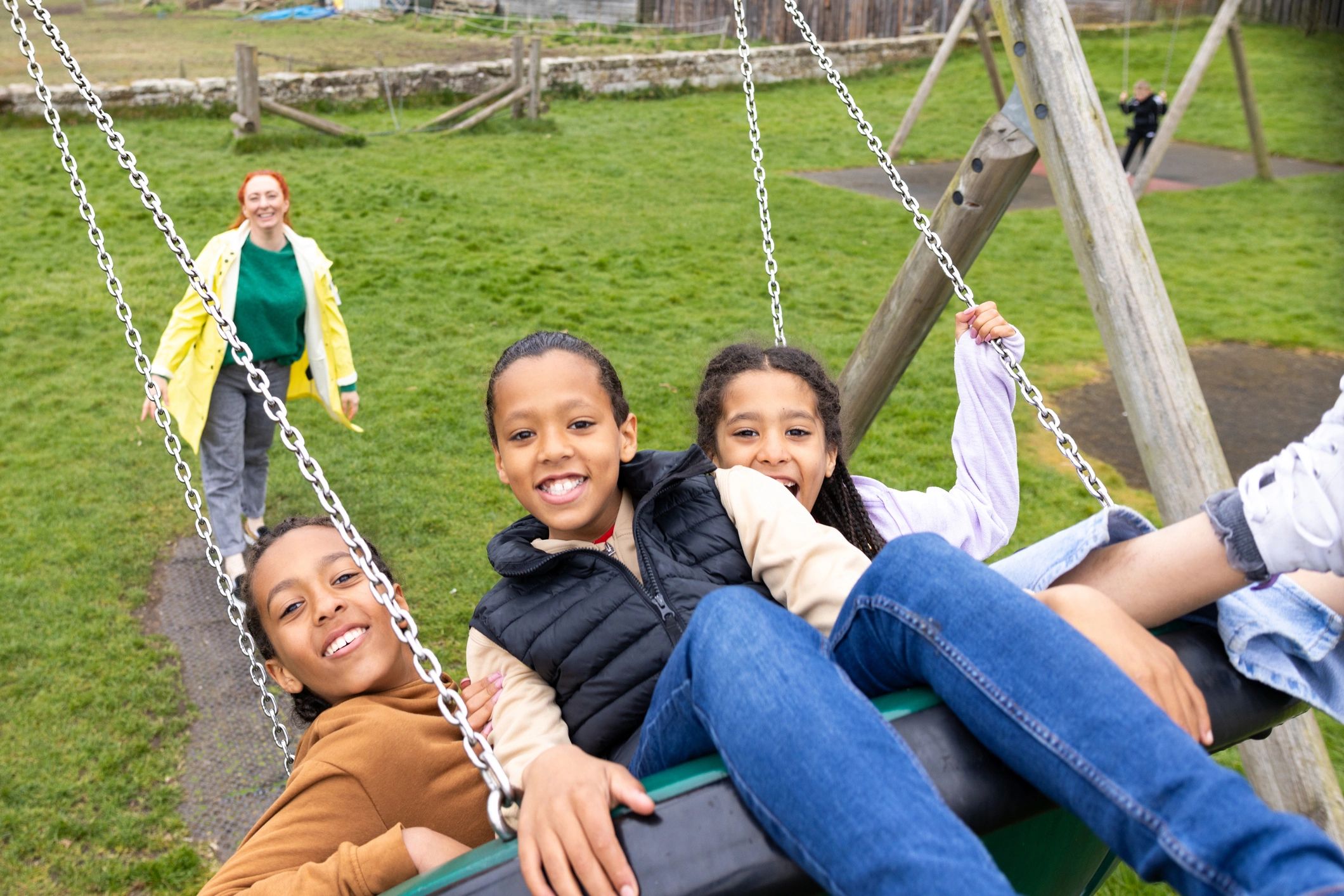 Children playing together on a playground swing with a parent nearby