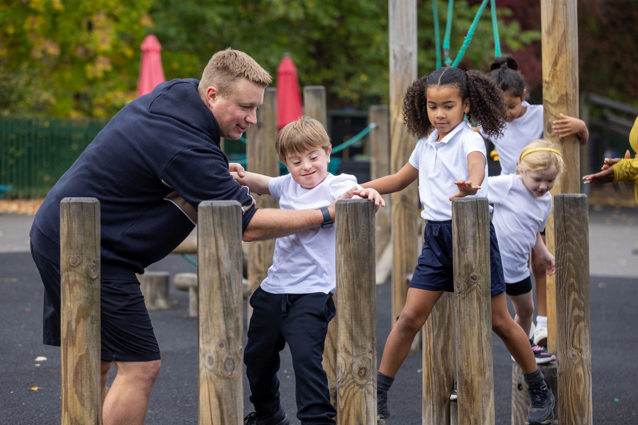 Children practicing balance and coordination on an outdoor obstacle course with teachers nearby