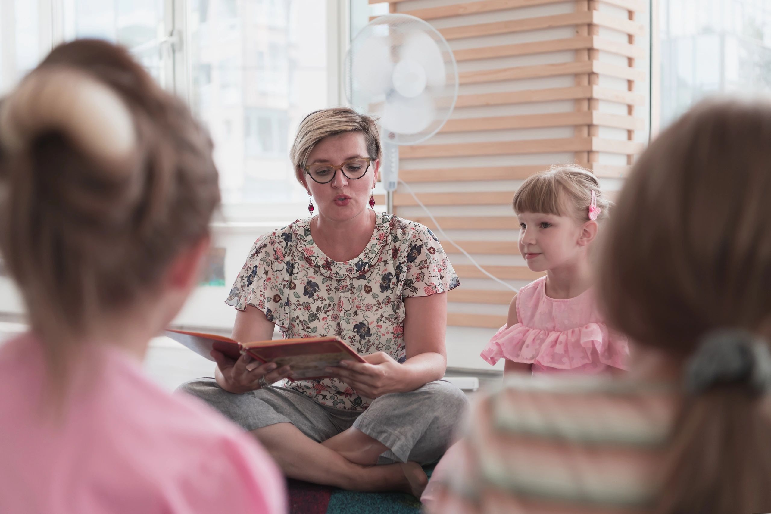 Teacher reading a book to a small group of children in a bright classroom
